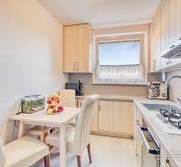 Kuchyně ve 4-pokojovém bytě s jídelním stolem, krémovými židlemi a kuchyňskou linkou.