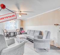 Obývací pokoj ve 4pokojovém bytě s pohodlnými křesly a jídelním koutem.