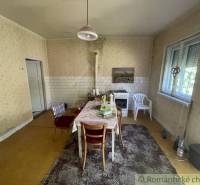 Jídelna v rodinném domě s kuchyňským stolem a kobercem, klasická atmosféra.