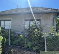 Rodinný dům v Tvrdošovcích s plotem a zelení, jasná slunečná obloha.