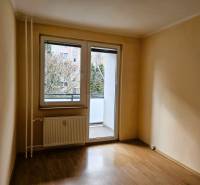 Prázdný pokoj v 3-pokojovém bytě s podlahou s dřevěným dekorem a prosklenými dveřmi na balkon.