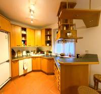 Kuchyně v 3-pokojovém bytě s dřevěnými skříňkami a barovým pultem.