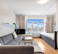 Obývací pokoj s pohovkou, závěsem a televizí, podlaha s dřevěným dekorem.