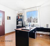 Kancelář s počítačem, policí a oknem s vertikálními žaluziemi v obchodních prostorách.