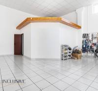 Obchodní prostory s bílými stěnami a keramickou podlahou. Součástí je uložené zboží.