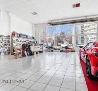 Autoservisní obchodní prostory se sklem a vystaveným autem na dlažbě, součástky na stěnách.