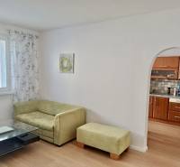 Obývací pokoj ve 3-pokojovém bytě s pohovkou, stolkem a obloukem do kuchyně.