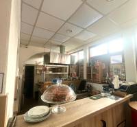 Interiér gastro prostoru s podlahou s dřevěným dekorem, pultem, zákuskem a talíři.