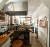 Kuchyňský prostor s nerezovým digestořem a podlahou s dřevěným dekorem v gastro prostorech.