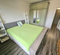 Ložnice v třípokojovém bytě s podlahou s dřevěným dekorem a zelenou postelí.