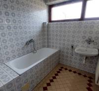 Koupelna s obklady se vzorem, vanou, umyvadlem a radiátorem v rodinném domě.