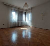 Prostorný pokoj s podlahou s dřevěným dekorem, bílými stěnami a záclonami v rodinném domě.