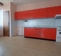 Kuchyně s červenými skříňkami, sporákem a oknem v rodinném domě.