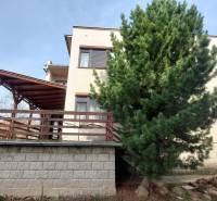 Rodinný dům ve Zlatých Moravcích s dřevěnou terasou, vysokým stromem a zahradou.