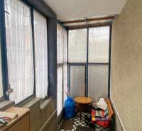 Prosklená veranda s modrým rámováním, šachovnicová podlaha a jednoduchý nábytek.