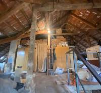 Podkroví rodinného domu s dřevěnými trámy, šikmou střechou a uskladněnými věcmi.