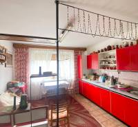 Červená kuchyňská linka v rodinném domě s dekorativním závěsem a puntíkovaným kobercem.