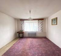 Pokoj v rodinném domě s fialovým kobercem, květinovými závěsy a lustrem.