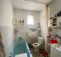 Koupelna v rodinném domě s vanou, pračkou a oknem.