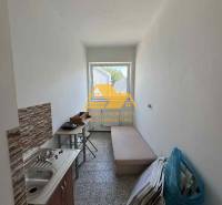 Malá garsonka s umyvadlem, stolem a lehátkem, vhodná pro praktické bydlení.