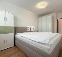 Světlý pokoj v rekreačním apartmánu s postelí, šatníkovými skříněmi a podlahou s dřevěným dekorem.