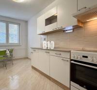 Světlá kuchyně v Rekreačním apartmánu s sporákem a stolem se zelenými židlemi.