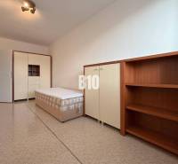 Světlá místnost v Rekreačním apartmánu s postelí, skříní a policovou sestavou.