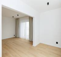 Pokoj v 3-pokojovém bytě s podlahou s dřevěným dekorem, závěsy a francouzským oknem.