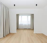 Pokoj v 3-pokojovém bytě s podlahou s dřevěným dekorem a velkými okny se závěsy.