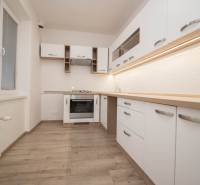 Kuchyně se spotřebiči, bílými skříňkami a podlahou s dřevěným dekorem v 2-pokojovém bytě.