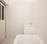 Koupelna v 2-pokojovém bytě s bílými obklady, umyvadlem a vanou.