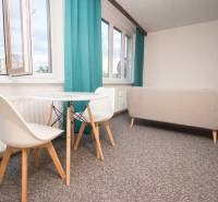 Obývací pokoj se stolem a židlemi ve 4pokojovém bytě, zářivé závěsy, světlý koberec.