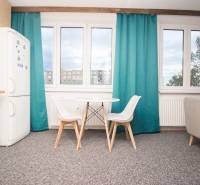 Kuchyně se stolem a židlemi ve 4pokojovém bytě, skříň a okna s tyrkysovými závěsy.