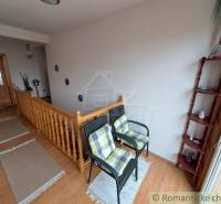 Interiér rodinného domu se schodištěm, židlemi a podlahou s dřevěným dekorem.