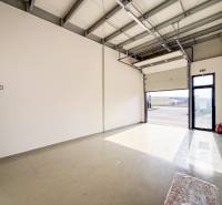 Obchodní prostory s velkou garážovou bránou a šedou podlahou s osvětlením.