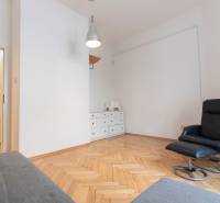 Interiér 4-pokojového bytu s křeslem, bílou komodou a podlahou s dřevěným dekorem.