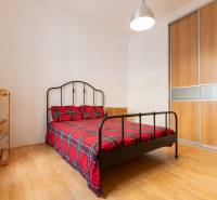 Ložnice ve 4pokojovém bytě s kovovou postelí, šatní skříní a podlahou s dřevěným dekorem.