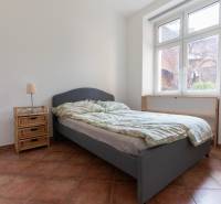 Ložnice ve 4pokojovém bytě s postelí, nočním stolkem a velkým oknem.