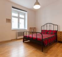 Ložnice ve 4pokojovém bytě s postelí, nočními stolky a podlahou s dřevěným dekorem.