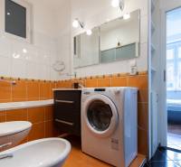 Koupelna s vestavěnou pračkou a oranžovým obkladem ve 4-pokojovém bytě.
