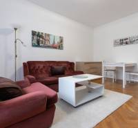 Obývací pokoj dvoupokojového bytu s bordovou pohovkou, bílým stolkem na podlaze s dřevěným dekorem.