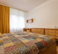 Ložnice v dvoupokojovém bytě se žlutými závěsy a dřevěným nábytkem.