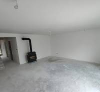 Interiér rodinného domu s krbem a schodištěm, čekající na dokončení.