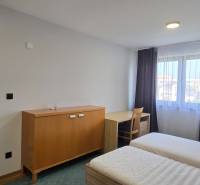 Ložnice s postelemi a nábytkem v třípokojovém bytě, bílé stěny, podlaha s dřevěným dekorem.