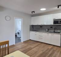 Kuchyně s bílými skříněmi a spotřebiči v 3-pokojovém bytě, podlaha s dřevěným dekorem.