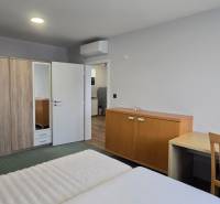 Ložnice v třípokojovém bytě s manželskou postelí, skříní a stolem.