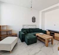 Obývací pokoj s tmavou pohovkou v 3pokojovém bytě s dlažbovou podlahou a dřevěným dekorem nábytku.