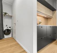 Kuchyň v 1-pokojovém bytě s podlahou s dřevěným dekorem a pračkou s poličkou.