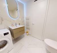 Koupelna v 1-pokojovém bytě s pračkou, umyvadlem a keramickými obklady.