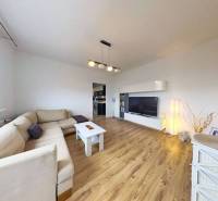 Obývací pokoj s podlahou s dřevěným dekorem v 3-pokojovém bytě se světlou sedačkou a TV skříňkou.